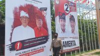 20200928_202606 SEORANG polisi melintas di depan baliho paslon Pilkada Denpasar yang dipasang di depan kantor KPU Denpasar, Senin (28/9/2020). Foto: gus hendra