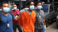 YONI Jatmiko (memakai baju tahanan) saat digiring anggota polisi YONI Jatmiko (memakai baju tahanan) saat digiring anggota polisi, di Mapolres Buleleng. Foto: rik