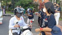 SEKRETARIS KPA Kota Denpasar, Tri Indarti, membagikan bunga mawar, pita red ribbon dan brosur terkait HIV/AIDS kepada pengendara yang melintas di perempatan Patung Catur Muka, Denpasar, Kamis (1/12/2022). Foto: tra