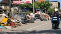 banjir denpasar SEORANG pemotor melirik ke tumpukan sampah bekas banjir bandang yang jejer di pinggir jembatan di Jalan Pulau Biak, Denpasar, Kamis (11/9/2025). Selain masalah sampah, banjir yang melanda Denpasar pada Rabu (10/9) lalu juga menyisakan lumpur dan debu di banyak jalan. Foto: gus hendra